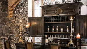 Un coin repas avec un mur en pierre, des chaises en bois, un buffet en bois foncé où sont rangées des bouteilles de vin, et une bougie sur la table.