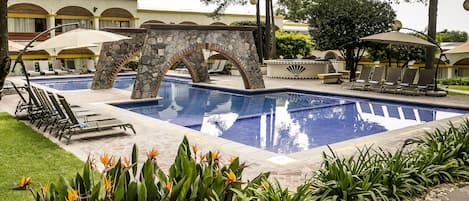 A swimming pool with lounge chairs and umbrellas, surrounded by greenery and a stone archway.