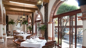 Un restaurant avec des tables dressées pour le service, des arches en briques et une vue sur un espace extérieur.