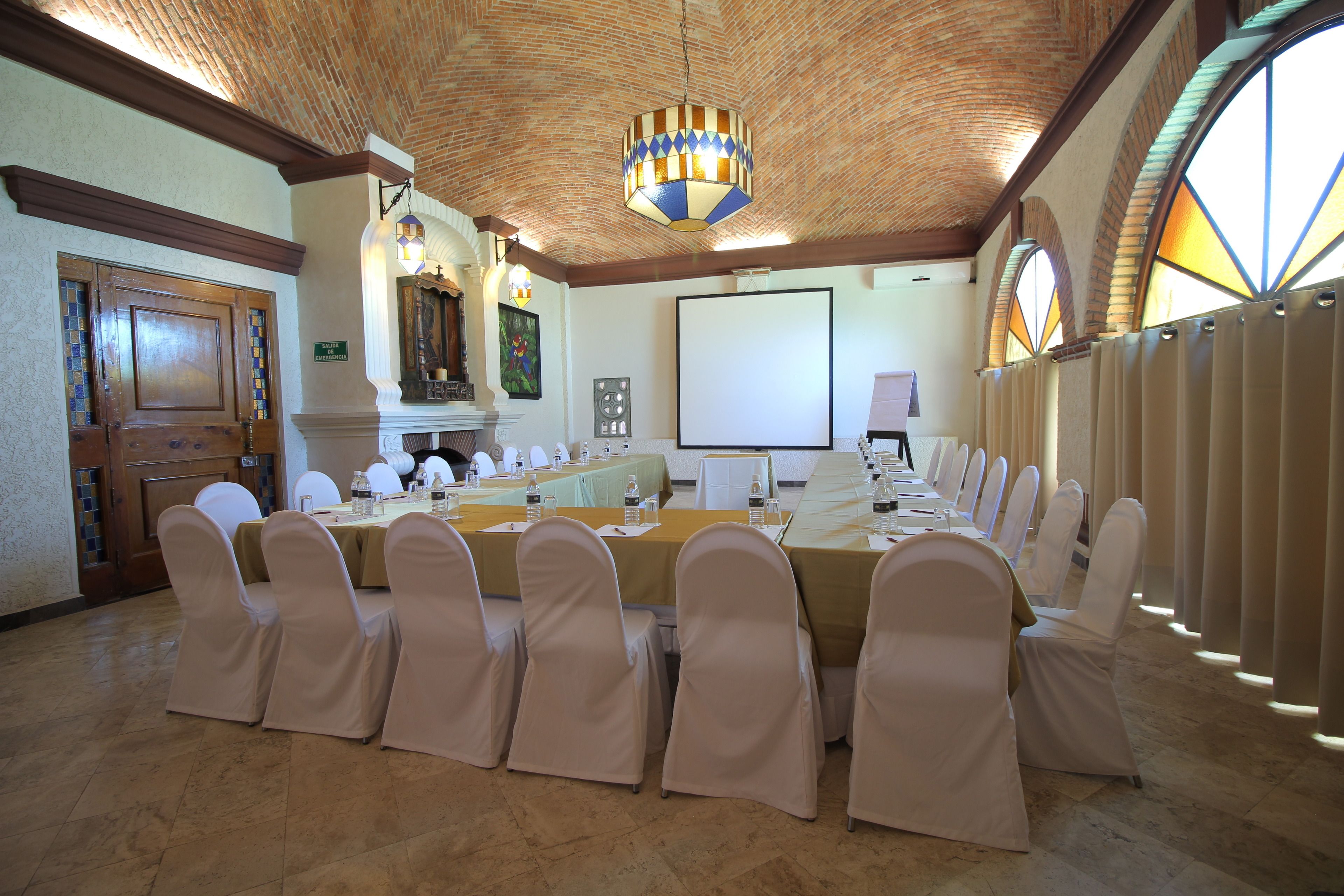 Un salón de conferencias con una larga mesa, sillas, una pantalla de proyector y una araña.