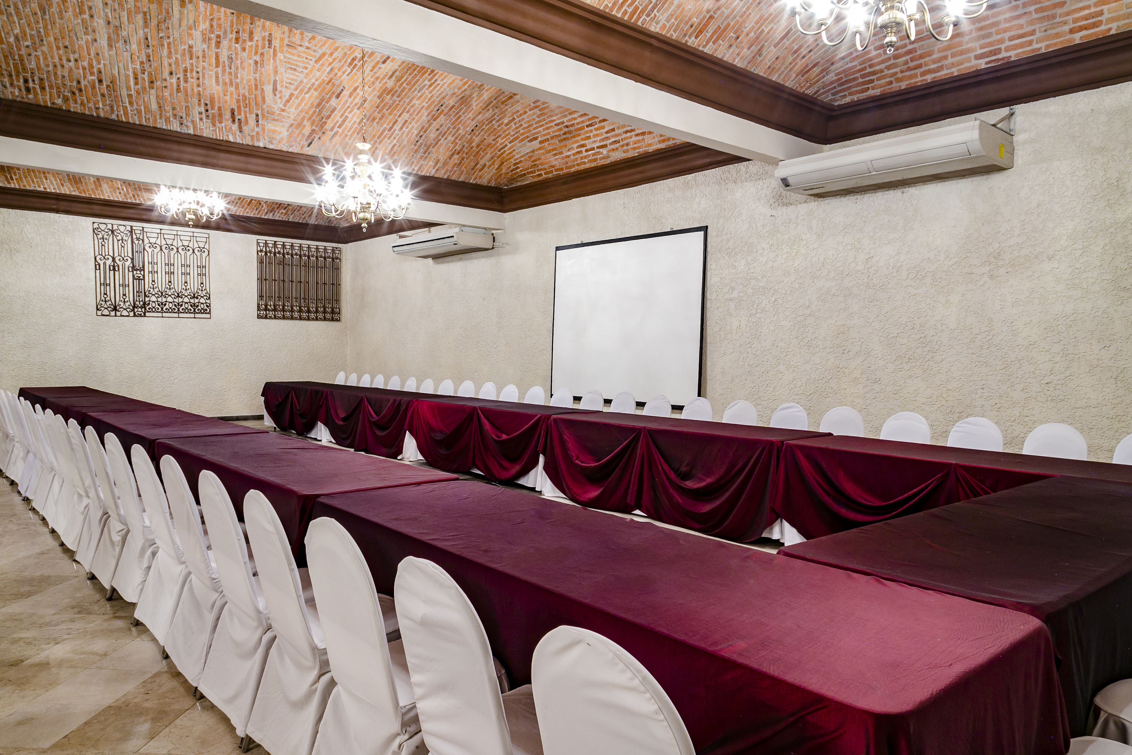 A conference room with a long table, white chairs, a whiteboard, and a brick ceiling.