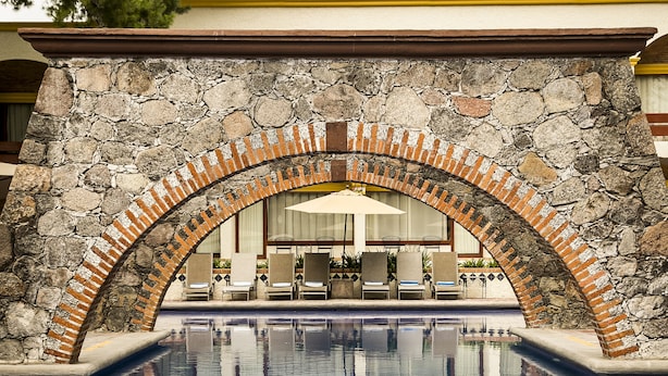 Un espace piscine agrémenté d’une arche en pierre, de chaises longues et offrant une vue sur la piscine.