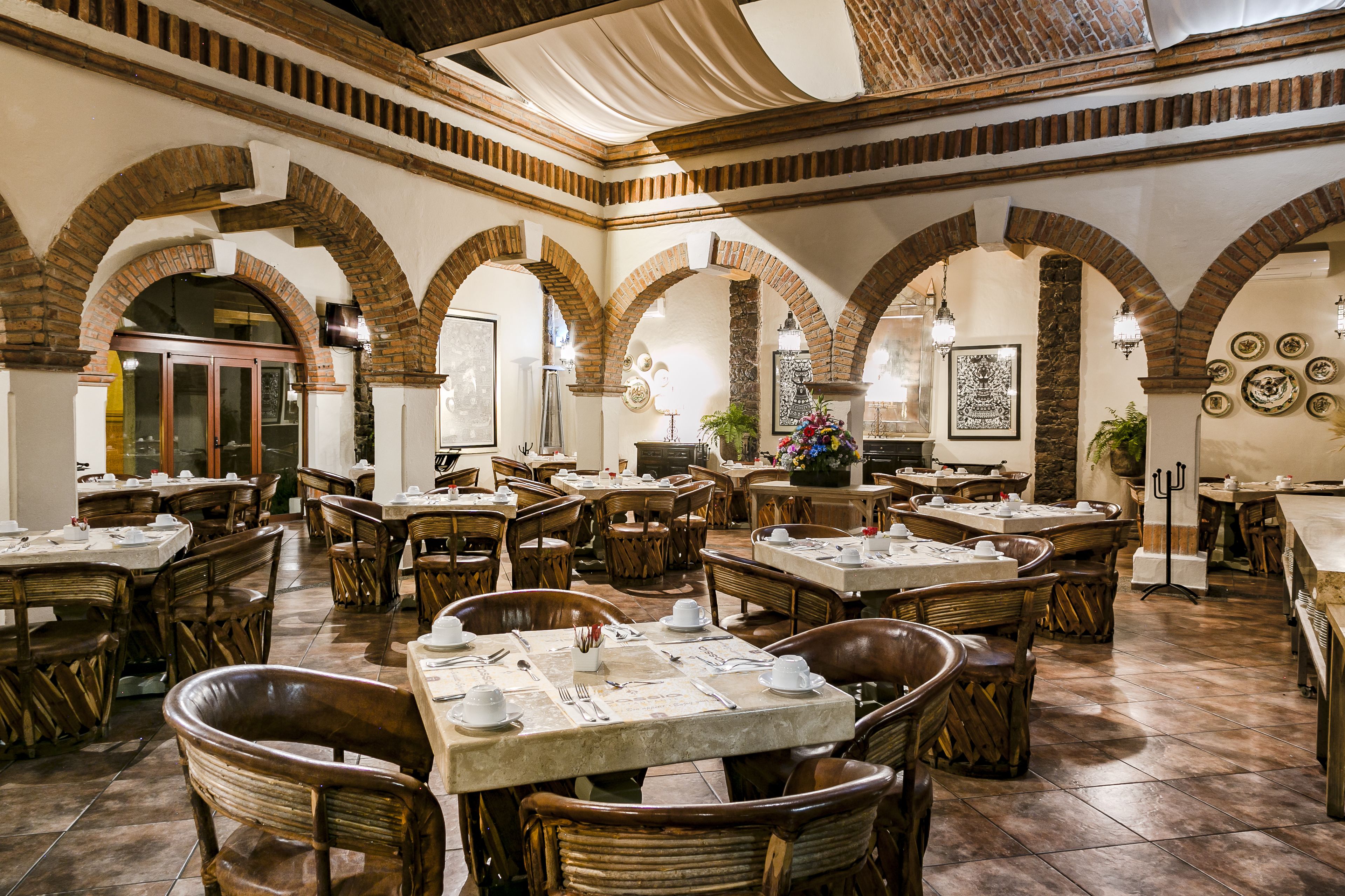Ein geräumiges Restaurant mit mehreren Tischen und Stühlen, Ziegelbögen und einem Fliesenboden.