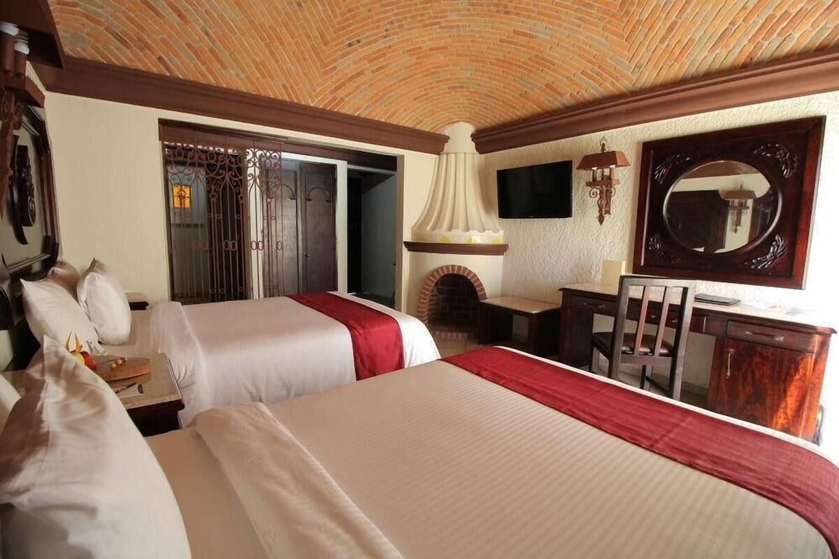 Ein Hotelzimmer mit zwei Betten, einem Schreibtisch, einem Sessel, einem Fernseher, einem Kamin und einem großen Spiegel.