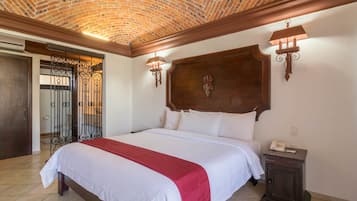 A hotel room with a large bed, a wooden headboard, two wall sconces, a bedside table with a phone, and a door with a wrought iron gate.