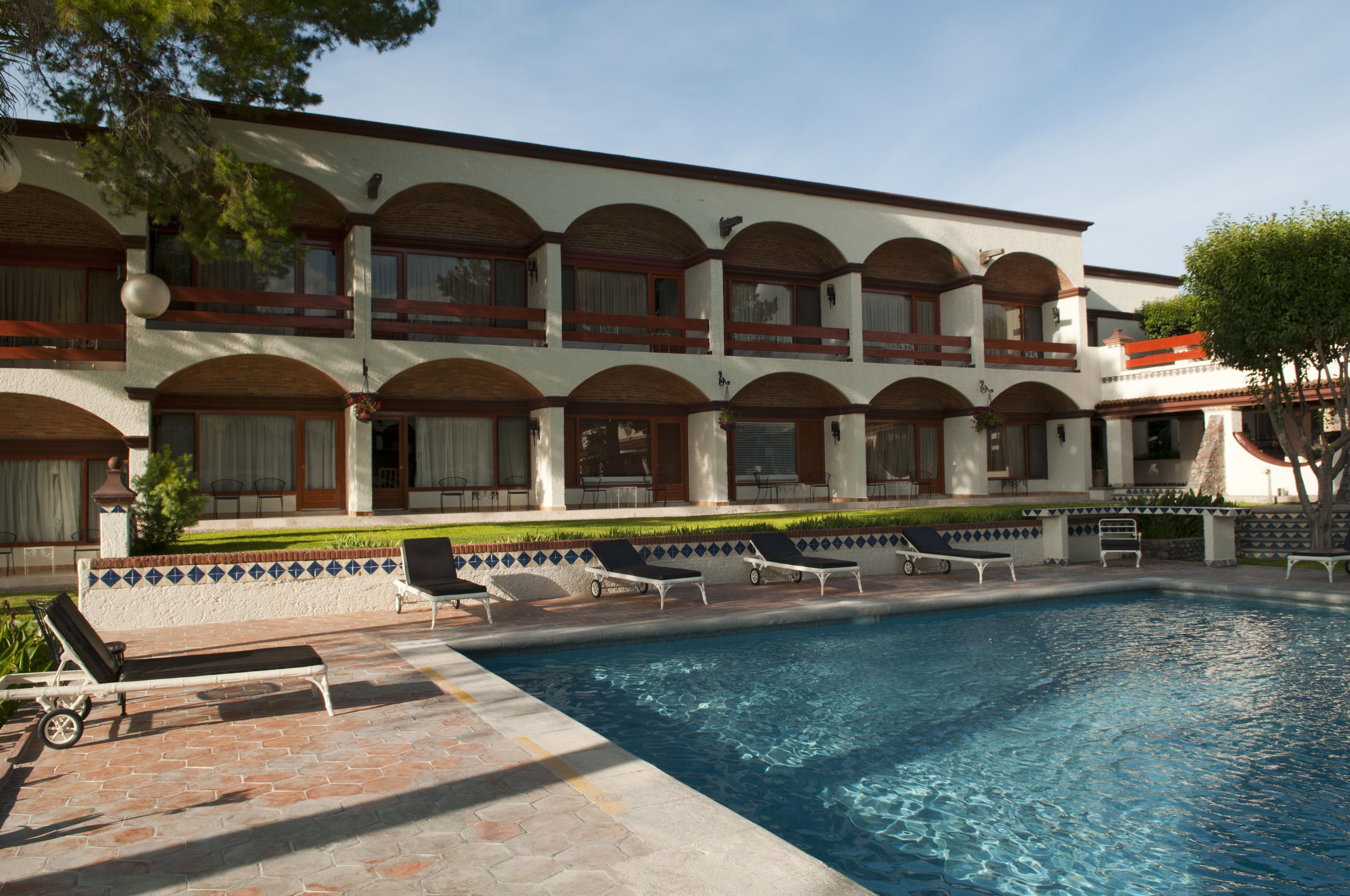 A hotel with a pool area, multiple lounge chairs, and a well-maintained garden.