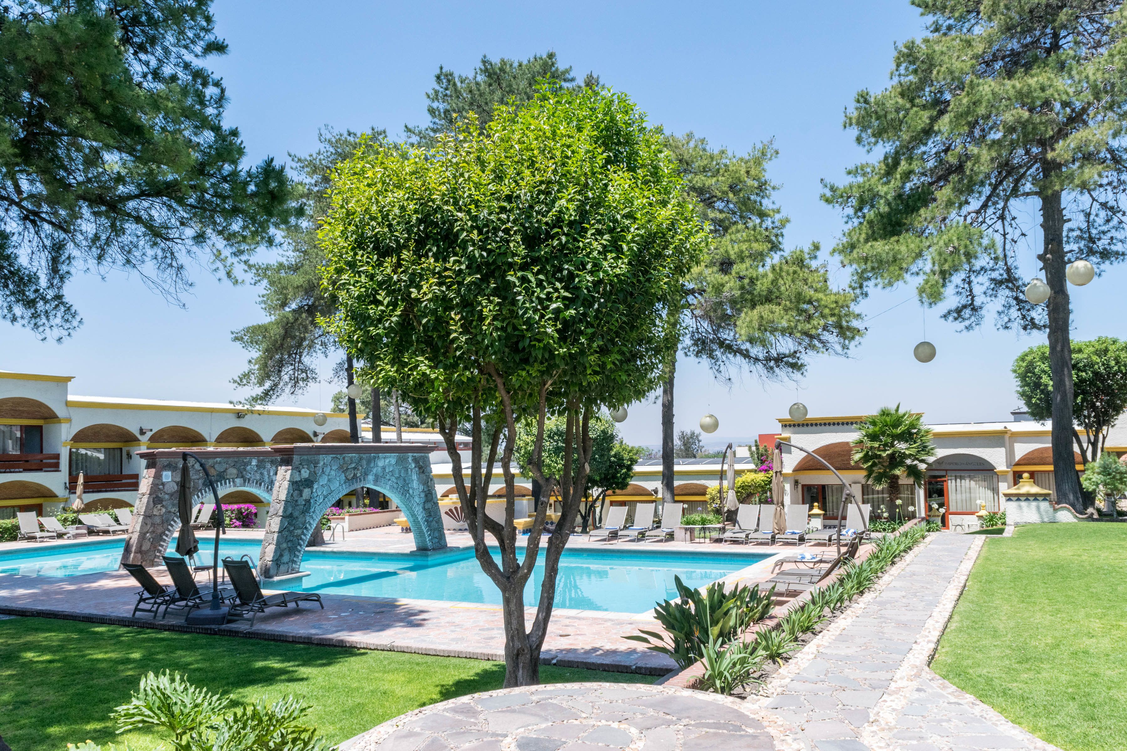 Un área de piscina con sillones de descanso, un arco de piedra y un césped cuidado.
