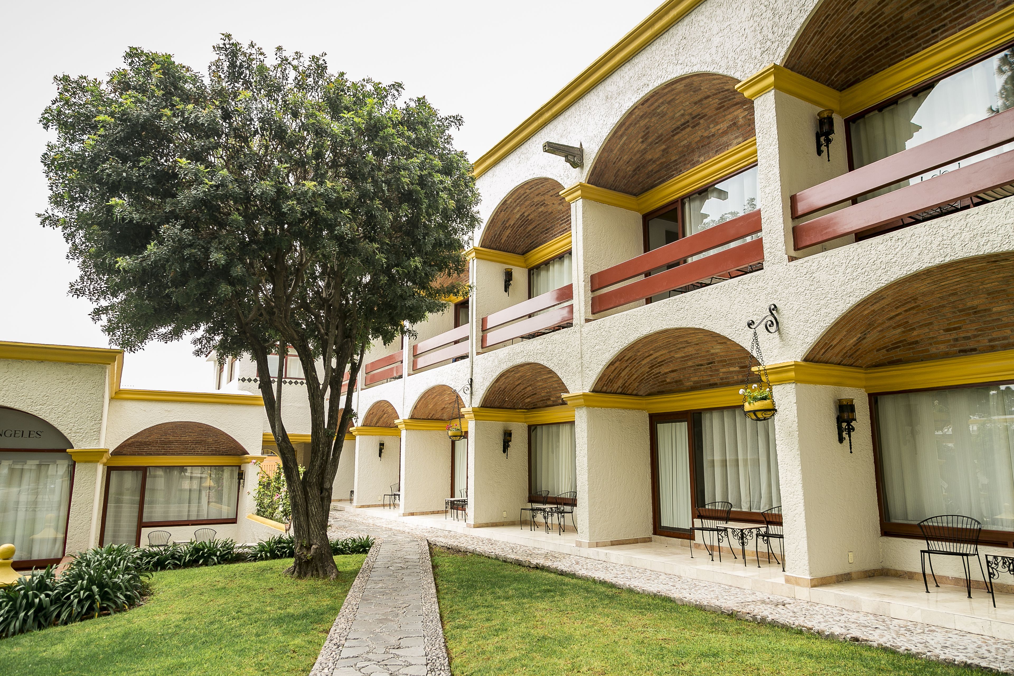 Un hotel con varios balcones, un camino central arbolado y zonas de estar al aire libre.