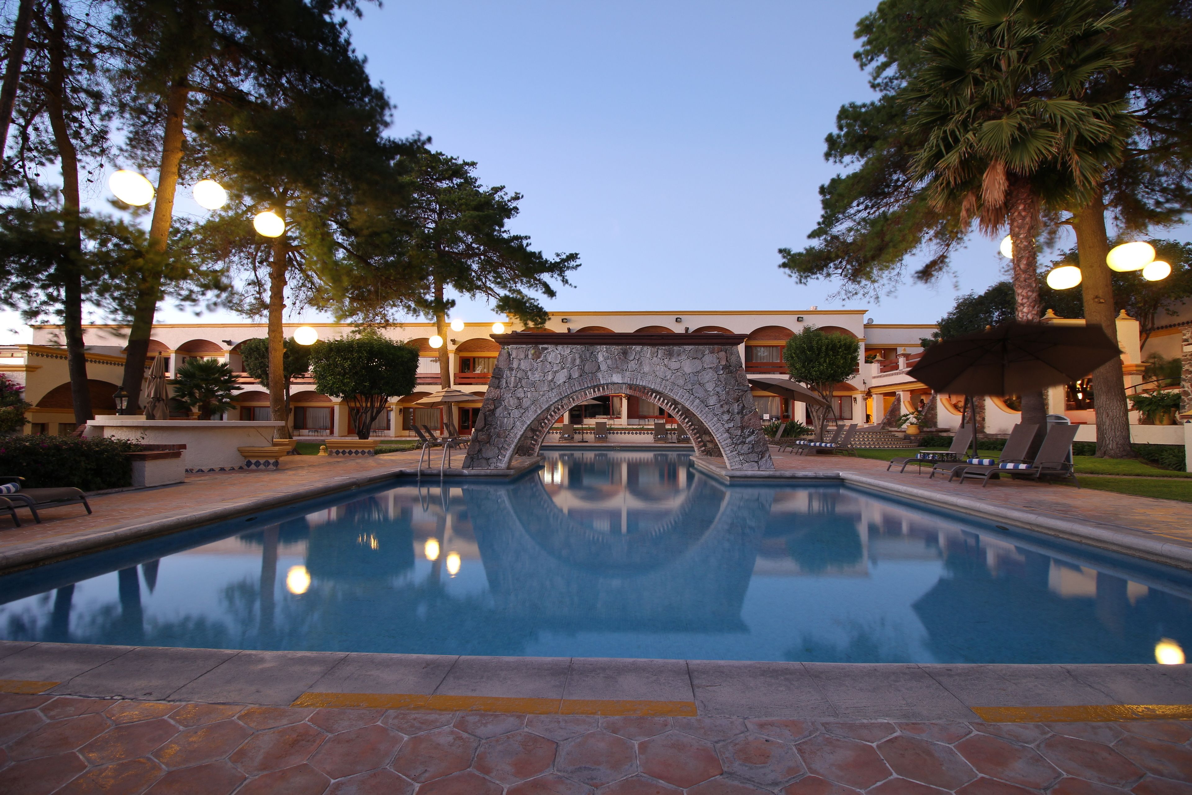 Ein Pool mit einem steinernen Bogen, umgeben von Palmen und Liegestühlen.