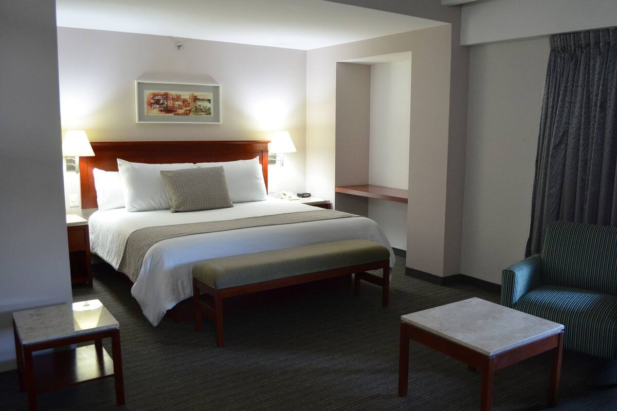 A hotel room with a bed, bedside tables, a bench, a chair, and a small table.