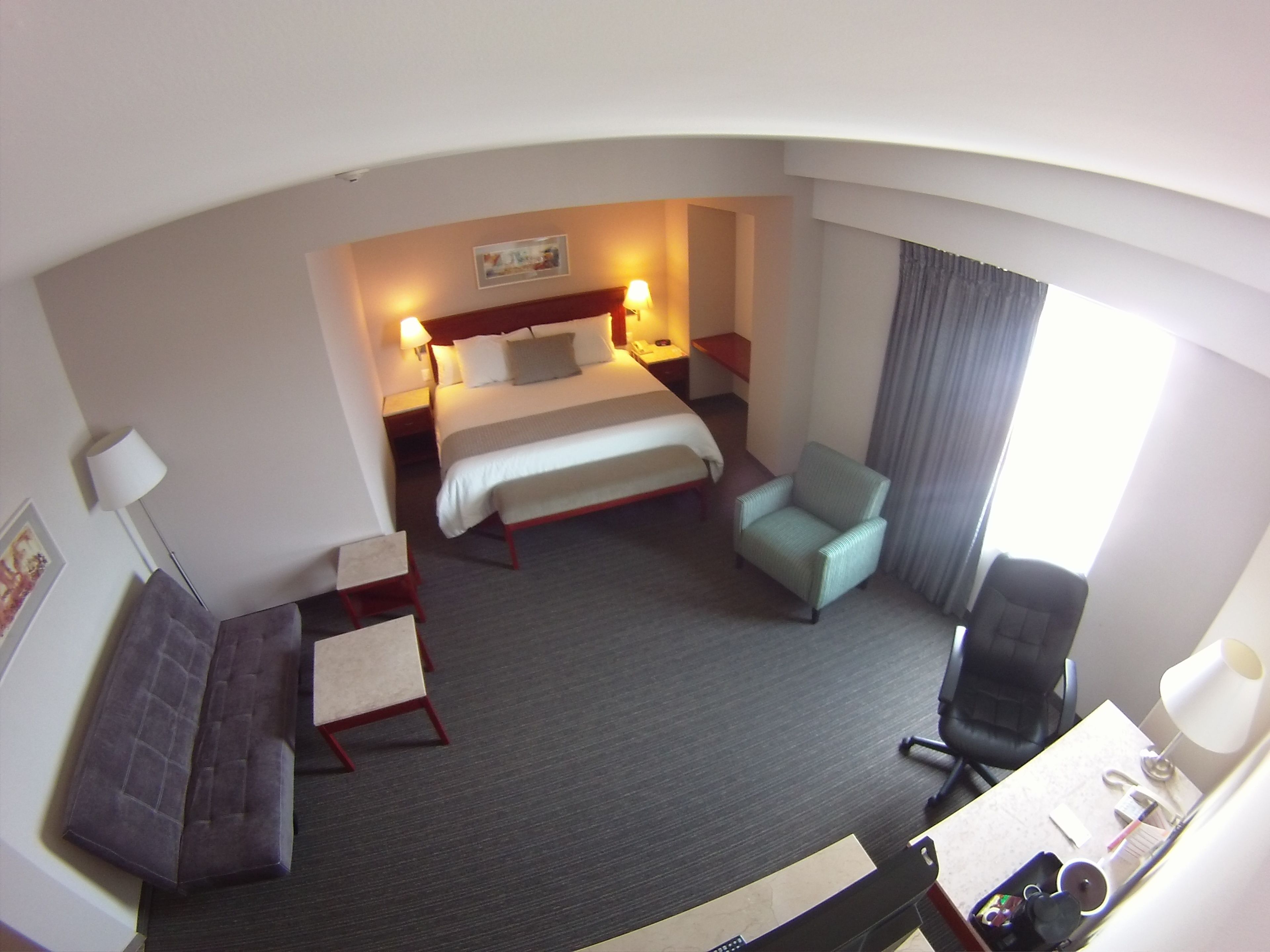 A hotel room with a bed, a desk with a chair, a sofa, and a window with curtains.