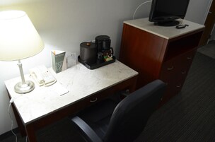 Habitación de hotel con escritorio, lámpara, cafetera, teléfono y televisor.