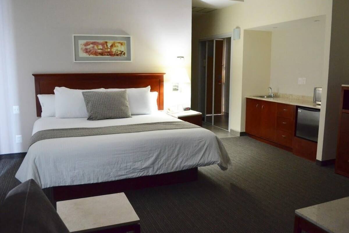 A hotel room with a bed, a desk, a kitchenette, and a bathroom.