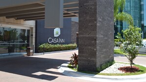 Um edifício moderno com a placa 'Casa Inn', apresentando um pilar de pedra, jardim ajardinado e um estacionamento.