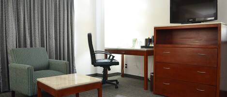 A hotel room with a single bed, a desk with a chair, a television, and a wooden dresser.