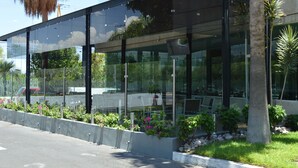 Um edifício moderno com fachada de vidro, área de estar externa e um jardim bem cuidado com diversas plantas e flores.