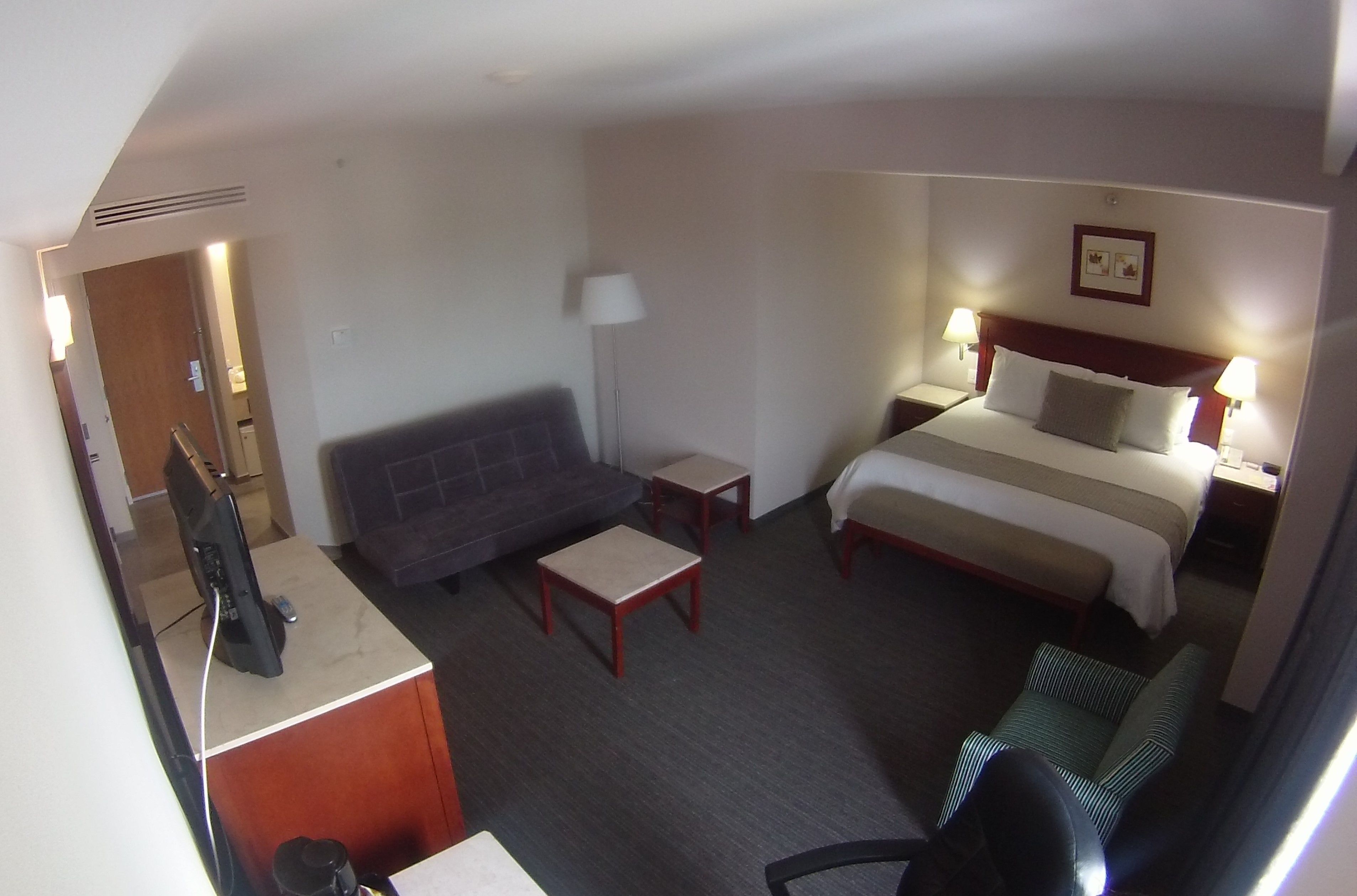 A hotel room with a bed, a sofa, a desk with a computer, a lamp, and a small table.