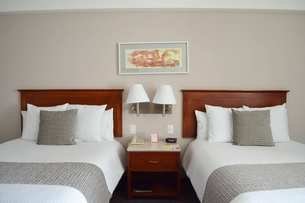 A hotel room with two beds, a nightstand with lamps, a framed picture on the wall, and a small table with a phone and a card.