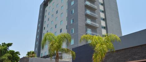 A high-rise hotel with a modern design, featuring balconies on each floor and a prominent logo on the facade.