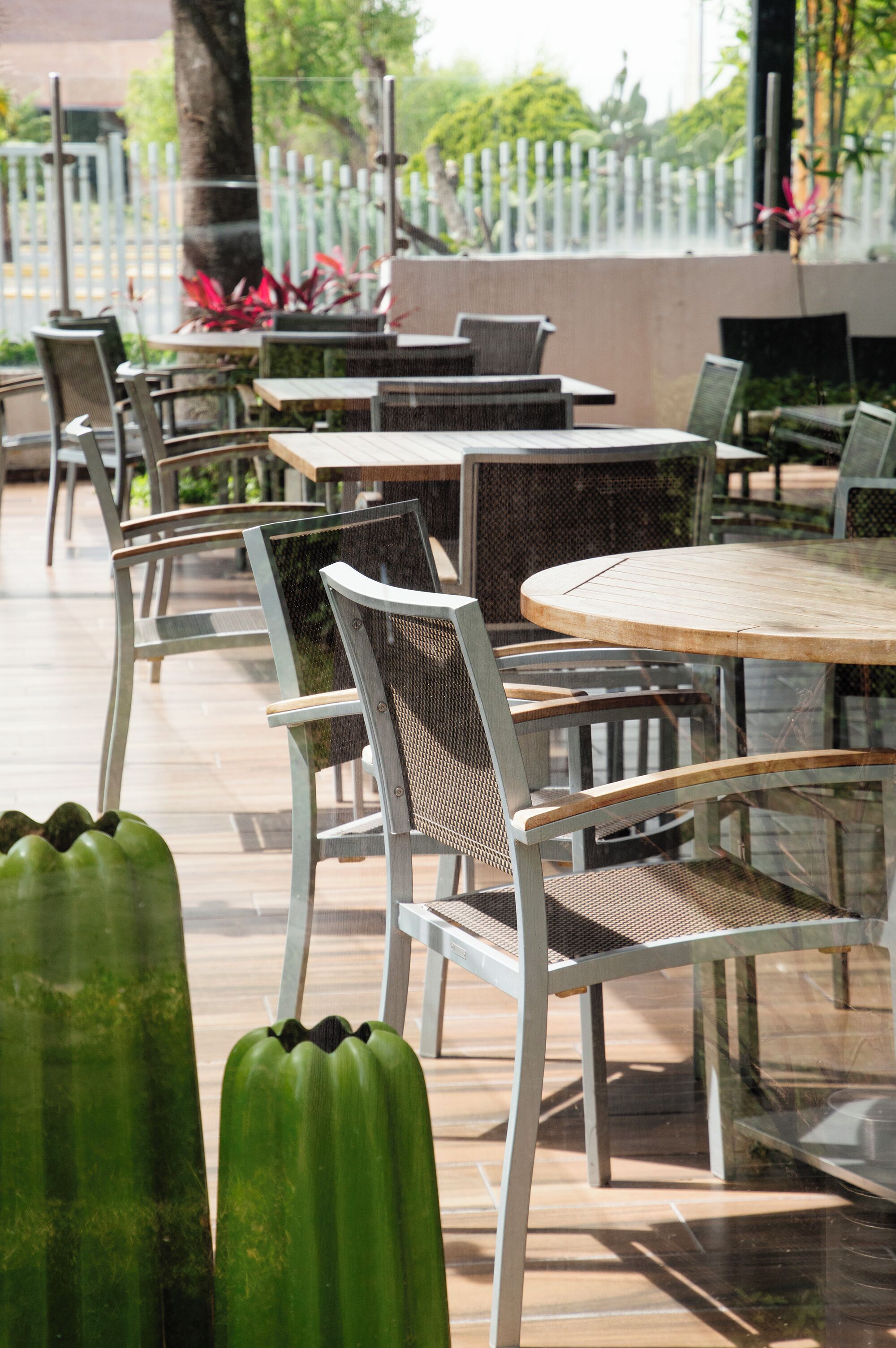 A patio area with round tables and chairs, surrounded by a white fence and greenery.
