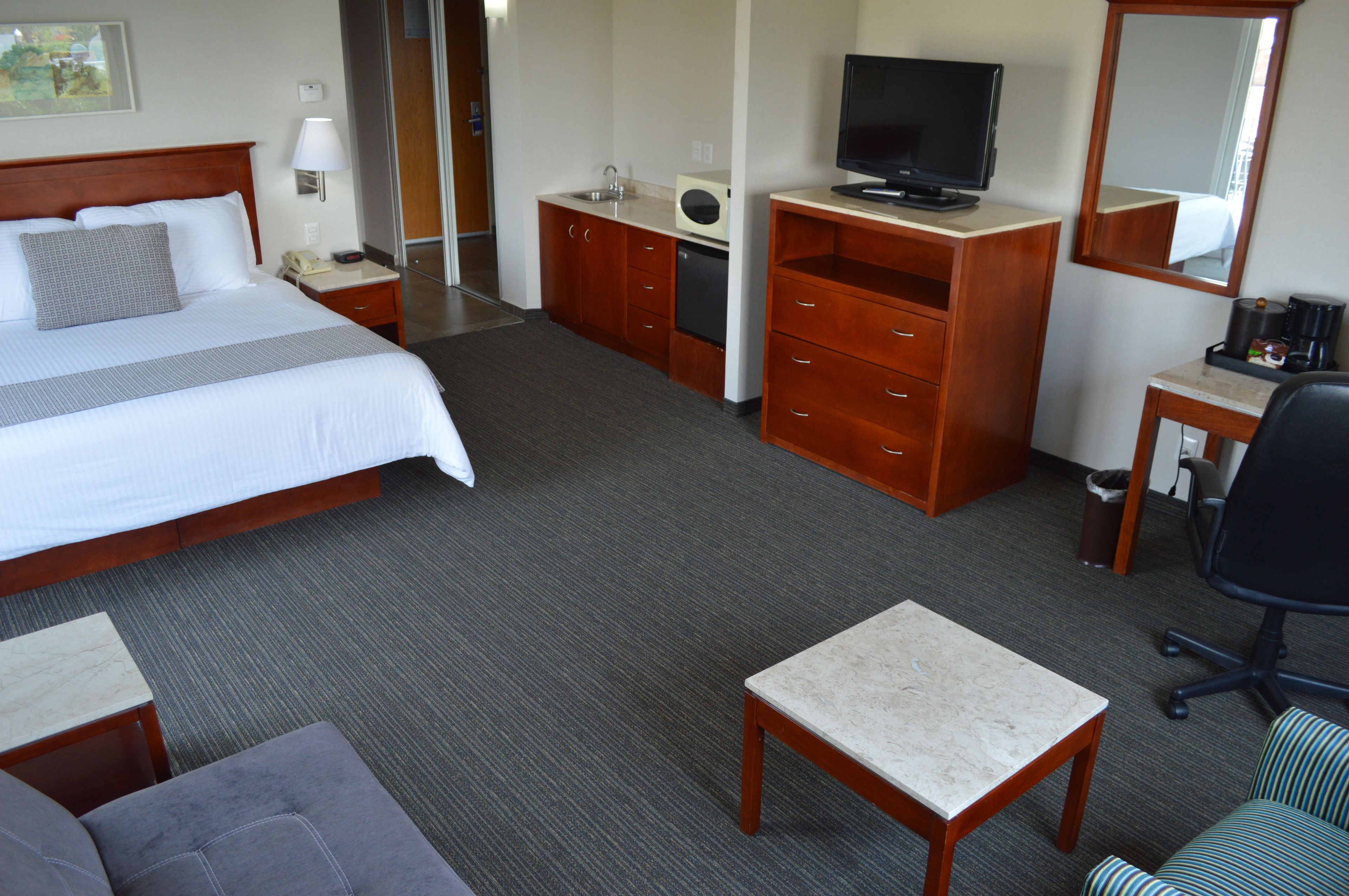 Una habitación de hotel con cama, escritorio, televisión, espejo y una pequeña mesa.