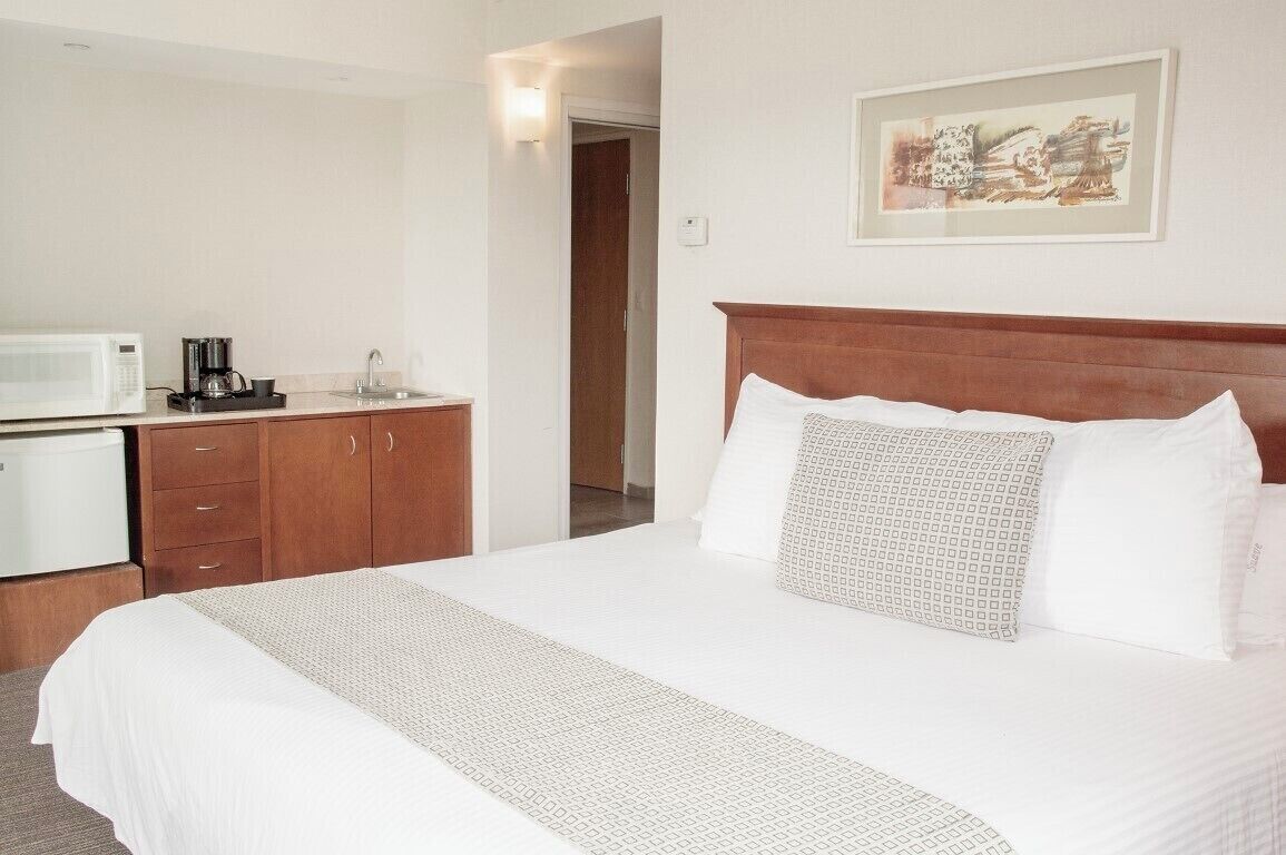 A hotel room with a bed, a microwave, a coffee maker, and a painting on the wall.
