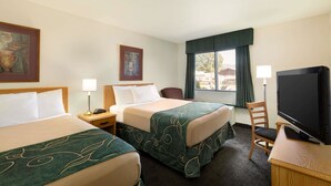 Una habitación de hotel con dos camas, un televisor, un escritorio con lámpara y una ventana con cortinas.