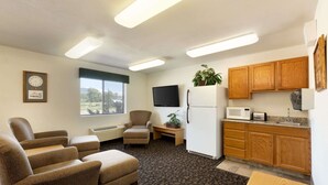 Un espacio habitable compacto con kitchenette, televisor de pantalla plana, refrigerador y una zona de estar con dos sillones y un sofá.