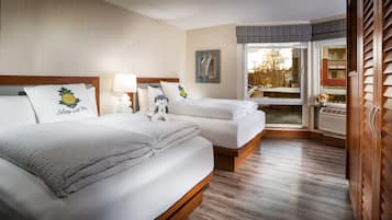 A hotel room with two beds, a large window with a view of the outside, and a wooden floor.