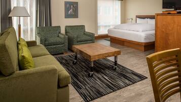 Habitación de hotel con cama, sofá, dos sillones, una mesa de centro de madera, lámpara y televisor.