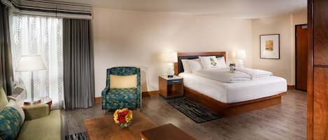 A hotel room with a bed, a sofa, a chair, a desk, and a lamp.