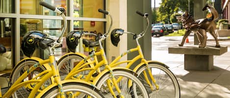 Una fila di biciclette gialle parcheggiate di fronte a un edificio con ampie finestre e una scultura in metallo a forma di cane.