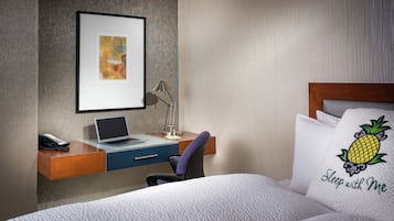 Et hotelværelse med en seng, et skrivebord med en bærbar computer, en telefon og et billede i ramme på væggen.