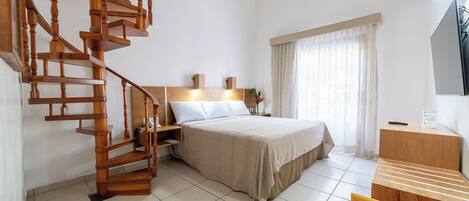 Quarto de hotel com escada em espiral de madeira, cama com cabeceira, escrivaninha e televisão.