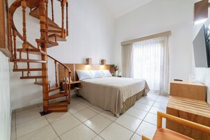 Habitación de hotel con una escalera espiral de madera, una cama con cabecera, un escritorio y un televisor.