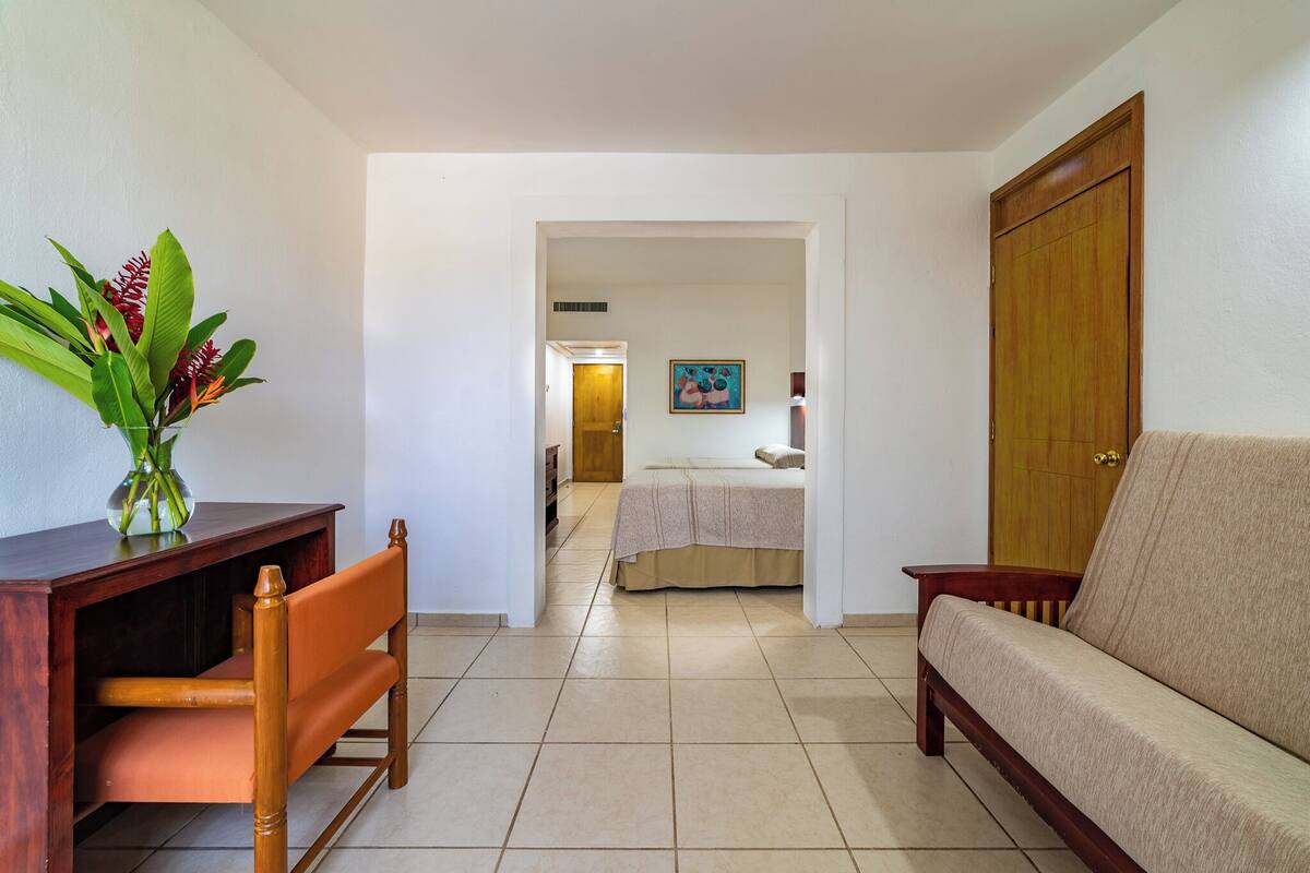 A room with a wooden desk, a sofa, a bed, and a door.