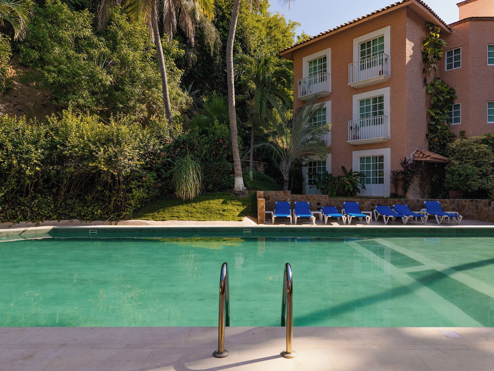 A swimming pool with blue lounge chairs and a building with balconies.