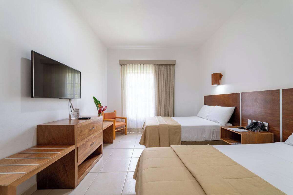 A hotel room with a flat-screen TV, wooden furniture, two beds, a desk, and a chair.