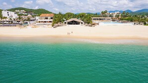 A beachside hotel with a pool, beach, and mountain backdrop.