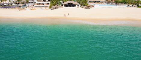 A beachside hotel with a pool, beach, and mountain backdrop.