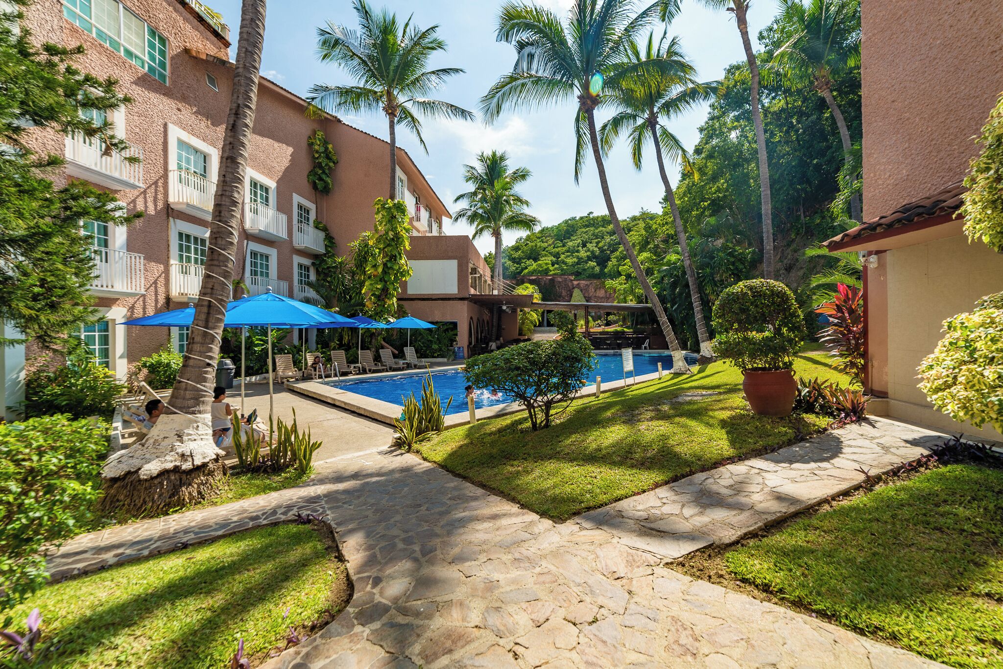 A pool area with a stone pathway, palm trees, and a building with balconies.