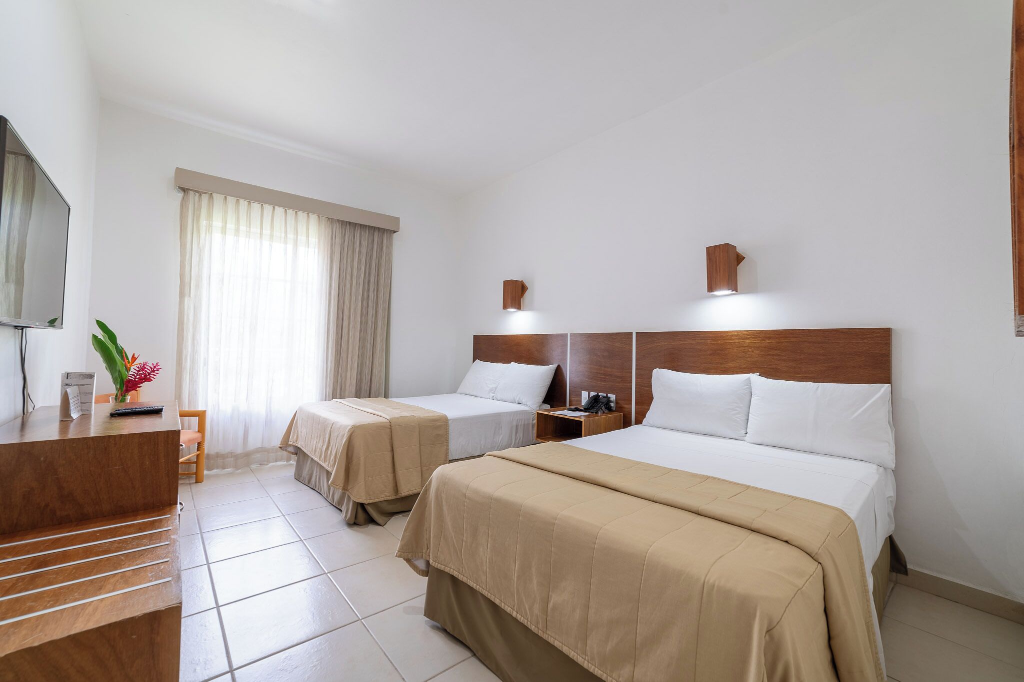 A hotel room with two beds, a desk, a chair, a TV, and a window with curtains.