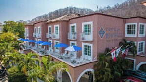 A hotel with a red facade, multiple balconies with white railings, and outdoor seating areas with blue umbrellas.