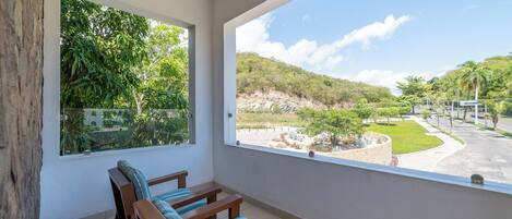Un balcon doté de mobilier en bois et offrant une vue sur un espace paysager agrémenté d’arbres et d’une route.