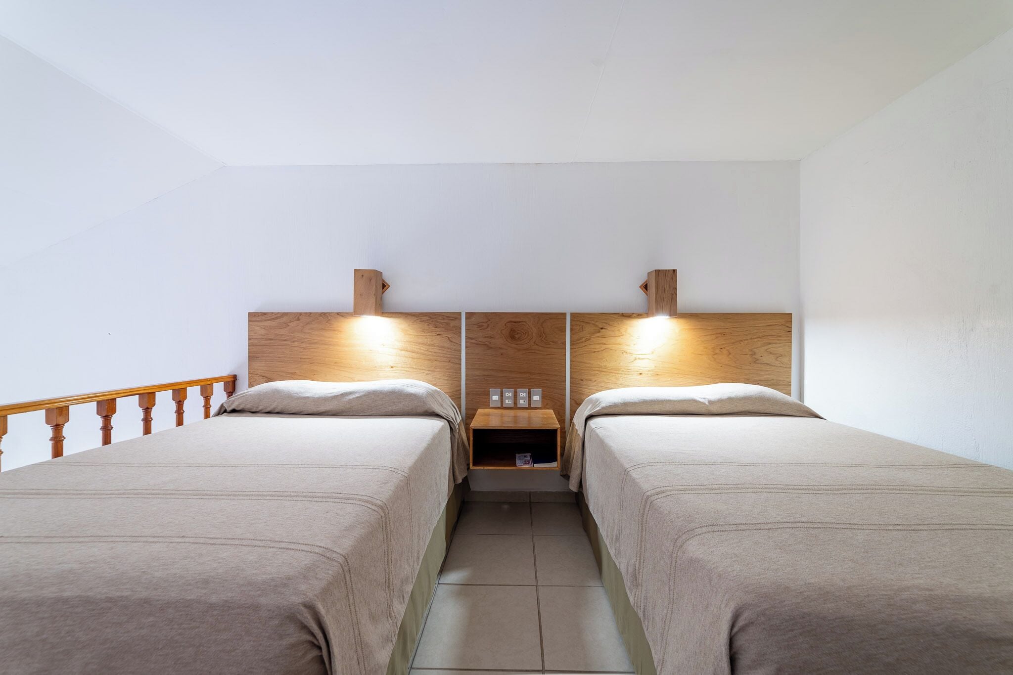 A twin room with two beds, wooden headboards, bedside tables, and a small shelf with a lamp.
