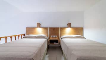 Habitación doble con dos camas, cabeceros de madera, mesitas de noche y una pequeña estantería con lámpara.