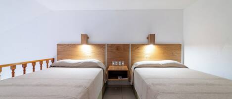A twin room with two beds, wooden headboards, bedside tables, and a small shelf with a lamp.