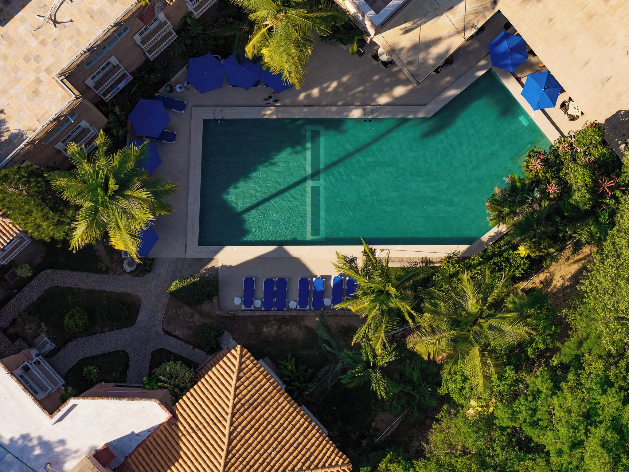 Eine Vogelperspektive eines Resorts mit Swimmingpool, Liegestühlen und Palmen.