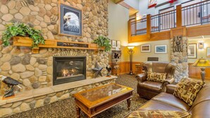A stone fireplace with a framed eagle picture, a leather armchair, and a glass coffee table in a lobby area. - Americinn By Wyndham Wabasha (Wabasha)