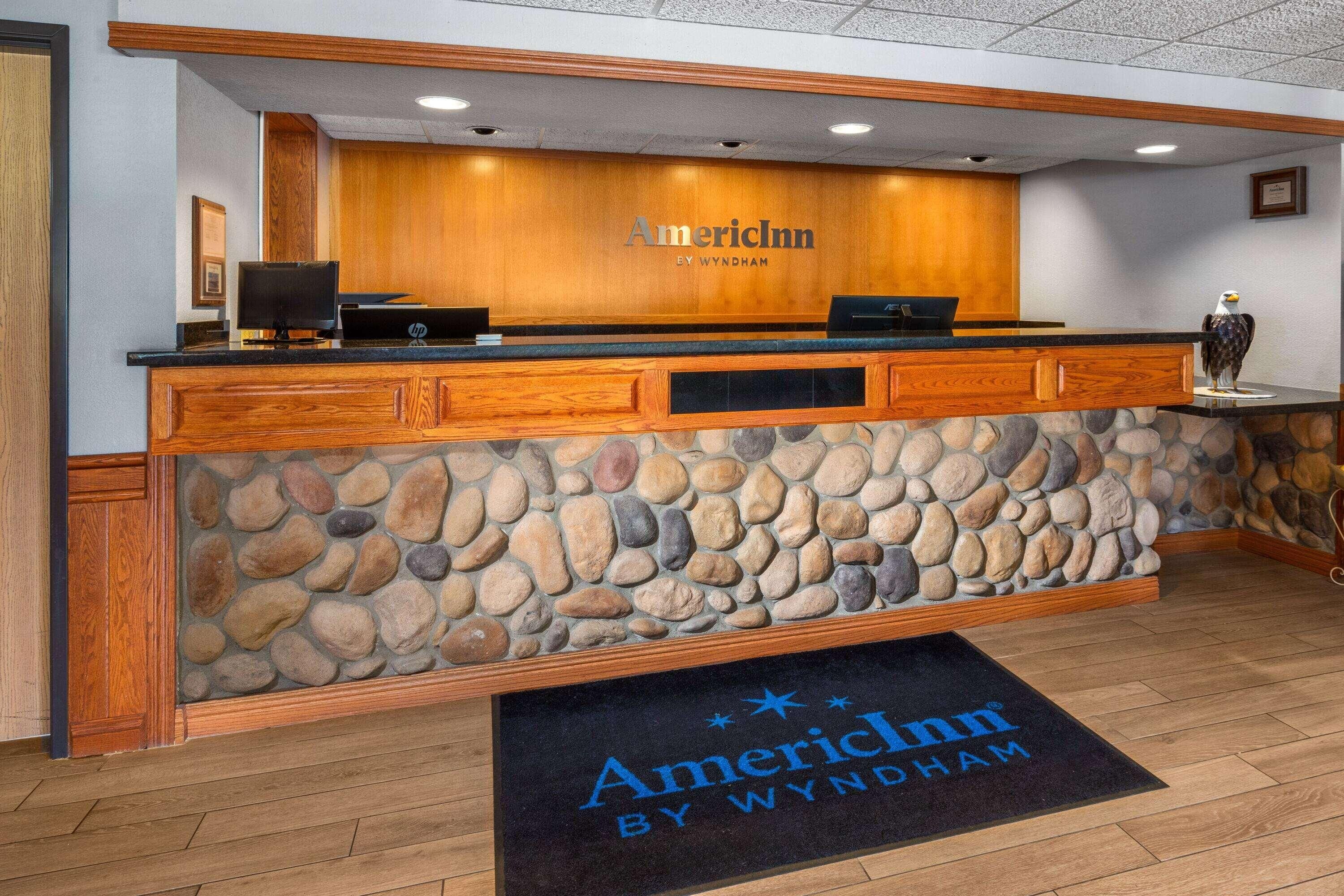 A reception desk with a stone facade, wooden paneling, and a logo for AmericInn by Wyndham.